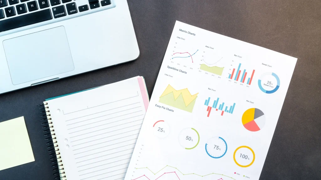 A laptop, notepad, and printed charts displaying analytics data, symbolizing SEO performance tracking and digital marketing analysis.